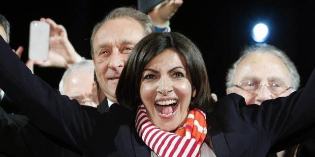 French Socialist Party deputy mayor of Paris, Anne Hidalgo, center, smiles, as outgoing mayor Bertrand Delanoe, stands behind her, during a speech after results were announced in the second round of the French municipal elections, in Paris, Sunday, March 30, 2014. Hidalgo saved Paris for the flagging Socialist Party in Sunday's municipal elections, becoming the French capital's first female mayor. (AP Photo/Thibault Camus)