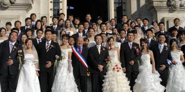 In this photo dated Oct. 2008, Tours mayor, Jean Germain, center, wearing a sash in the colors of the French flag, poses with a group of recently married Chinese couples in front of the city hall in Tours, France. Jean Germain the former mayor of Tours has been found dead in a suspected suicide right as he was to go on trial over suspected kickbacks involving a spate of group weddings of Chinese visitors in the picturesque Loire Valley city. A defense lawyer said a half-dozen people are on trial over alleged kickbacks linked to euro750,000 ($815,000) that the city spent from 2008 to 2011 to lure Asian visitors _ some for weddings presided over by Germain while he was mayor. (AP Photo/Patrice Deschamps, la Nouvelle Republique) FRANCE OUT