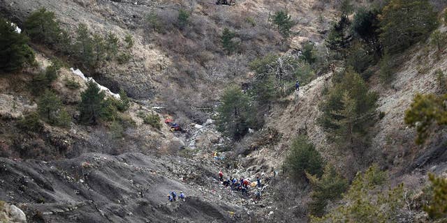 FILE - In this Thursday March 26, 2015 file photo, a helicopter flies over rescue workers at the crash site of the Germanwings jet near Seyne-les-Alpes, France. The somber mission to recover the remains of 150 people killed instantly when the Germanwings flight slammed full speed into the Col de Mariaud is not a quiet one and crucial physical evidence for the crash investigation can be gathered only when the mountains cooperate. (AP Photo/Laurent Cipriani, File)