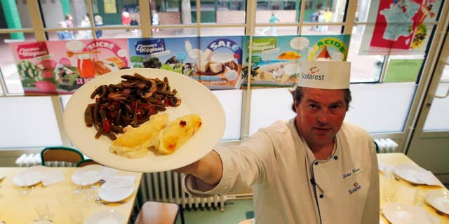 FOR STORY FRANCE SCHOOL LUNCHES - FILE - In this May 6, 2014 file photo, French chef Xavier Lebeau poses with a plate of Quenelles de Brochet (pike fish) with Green Haricot beans and Champignons de Paris (Paris mushrooms), at the Saint Pierre de Chaillot school in Paris, France. France has been grappling with how to reconcile religious beliefs with secular values when it comes to pork in school lunches, with one lawmaker’s solution: vegetarian meals. (AP Photo/Francois Mori, File)