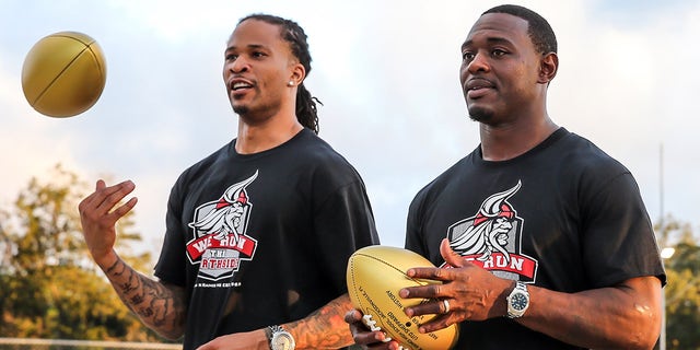 Former NFL players Jabar Gaffney, left, and Lito Sheppard present golden footballs during a Super Bowl High School Honor Roll ceremony at their alma mater William M. Raines High School in 2015