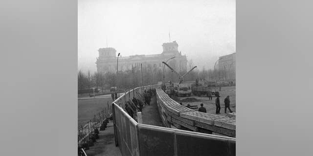FILE - The Nov. 20, 1961 photo shows 12 feet high boards hiding the work as East German troops erect a new concrete wall at the Brandenburg Gate, marking the East-West border in Berlin. In background is the former Reichstag building which is in West Berlin.  (AP Photo/file)