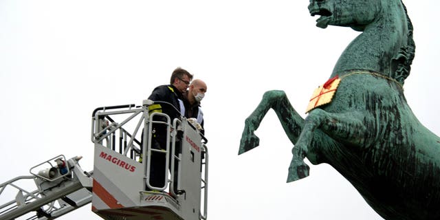 Feb. 5, 2013: A firefighter and a police officer look at a golden Leibniz cookie that hangs from a horses neck in front of the Leibniz University in Hannover, Germany.