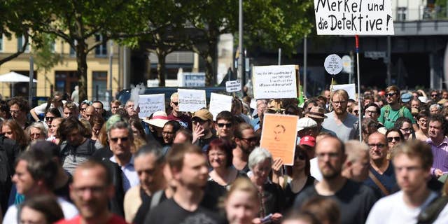 Participants of a demonstration protest in Berlin, Saturday Aug. 1, 2015. Banner at right reads "Merkel und die Detektive!" (lt: Merkel and the detectives). Some 1,300 people rallied in Berlin for the freedom of the press in support of two journalists who prosecutors are investigating for treason over two reports revealing authorities' plans to expand surveillance of online communication. Website Netzpolitik.org, which covers digital rights issues, said Thursday it was notified by federal prosecutors of the probe against its staff and an unidentified source over the two reports. (Britta Pedersen/dpa via AP)
