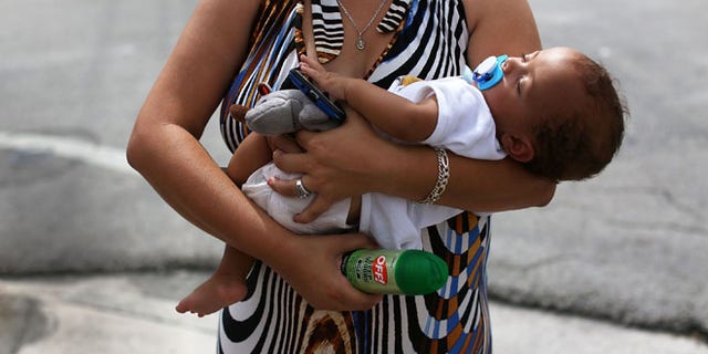 MIAMI, FL - AUGUST 02: Barbara Betancourt holds her baby Daniel Valdes after being given a can of insect repellent by James Bernat, a City of Miami police officer, as he helps people living around the Miami Rescue Mission prevent mosquito bites that may infect them with the Zika virus on August 2, 2016 in Miami, Florida. A reported 14 individuals have been infected with the Zika virus by local mosquitoes. (Photo by Joe Raedle/Getty Images)