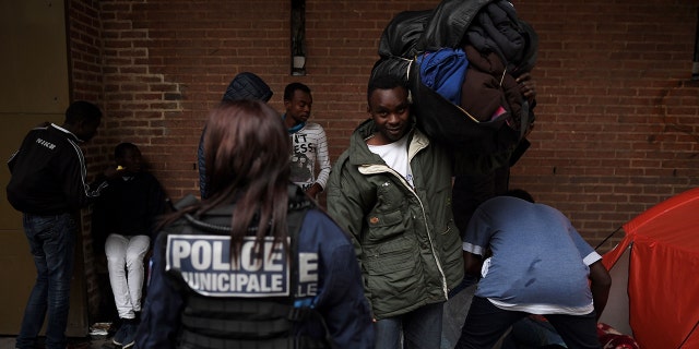 A police officer stands guard as migrants pack up their belongings after sleeping on the floor in Saint-Denis outside Paris on October 11, 2017.