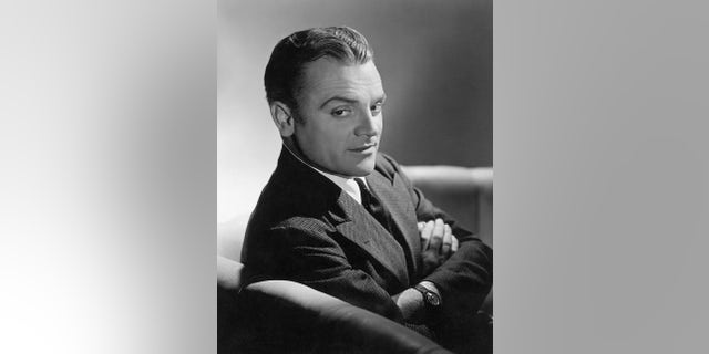 Close-up of actor James Cagney sitting on a sofa with his arms folded across his chest.