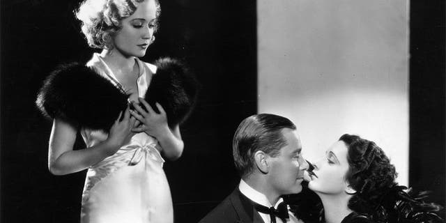 Miriam Hopkins (left) looks on while Herbert Marshall and Kay Francis share a romantic moment during the filming of Paramount's 1932 romantic comedy, "Trouble in Paradise", directed by Ernst Lubitsch.