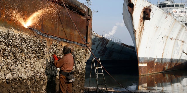 A worker uses a cutting torch to dismantle a barnacle-covered hull at the Galloo ship reycling plant in Belgium, Europe's largest