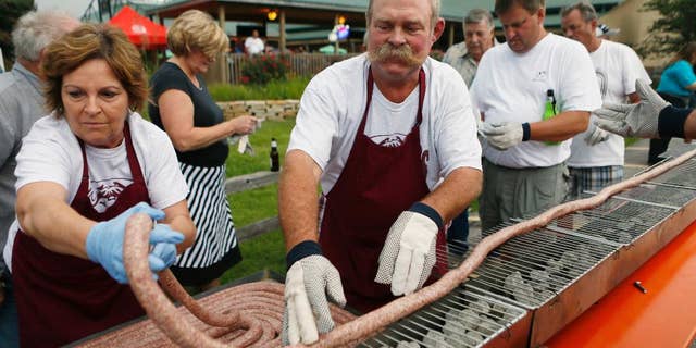 In this Tuesday, Sept. 9, 2014 photo, Mabel and Larry Schubert help lay out a 100 foot-long bratwurst on a grill at the Silver Creek Saloon in Belleville, Ill. About 50 people volunteered to carefully grill the bratwurst without burning or breaking it. The event was a practice run for the Belleville 200th celebration where they will be grilling a 200 foot-long bratwurst on Sept. 21. (AP Photo/Belleville News-Democrat, Zia Nizami)