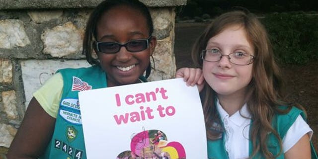In this Sept. 27, 2013 photo provided by the Girl Scouts, Natalie Harrison, left, and Jasmine Barnett of Troop 2424 hold a promotional poster for their organization outside of Matthews Elementary School in Charlotte, N.C. The fifth graders were volunteering at a Girl Scout Informational night at the school to share their stories about their experiences in the group. Instead of placing ads on TV, in newspapers and on billboards, a decentralized campaign aimed at reversing a long-running decline in participation in the Girl Scouts will unfold in neighborhood initiatives and on social media as local councils directly target elementary school girls - even kindergartners - with promises of adventuresome fun. (AP Photo/Girl Scouts, Colleen Young)