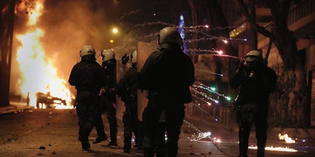 Greek riot police shelter from a flare thrown by rioting youths during clashes after a demonstration by about 700 anarchists seeking the abolition of a maximum security prison, in central Athens, on Tuesday, April 7, 2015. Dozens of rioters burnt at least two cars, smashed a shopfront and threw petrol bombs and stones at police, who responded with tear gas. Four suspected rioters were detained, while no injuries were reported. (AP Photo/Petros Giannakouris)