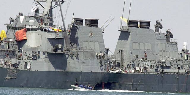 FILE -- In this Sunday Oct. 15, 2000 file photo, investigators in a speed boat examine the hull of the USS Cole at the Yemeni port of Aden, after a powerful explosion ripped a hole in the U.S Navy destroyer, killing at least 17 sailors and injuring some 30 others. Prosecutors are asking a military judge in Guantanamo Bay to reconsider his order that they share with defense attorneys details about a detainee’s experience in secret CIA prisons after he was arrested in connection with the deadly attack on the USS Cole in Yemen. (AP Photo/Dimitri Messinis, File)