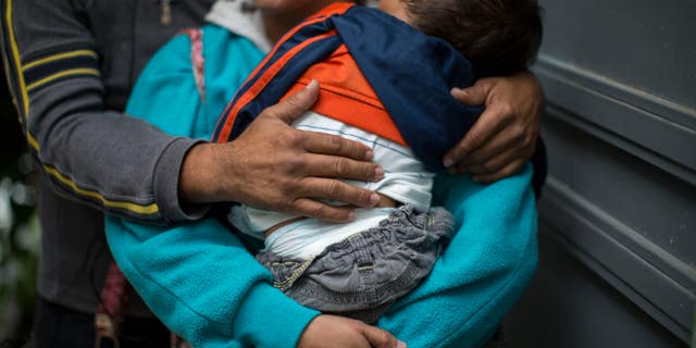 In this June 19, 2014 photo, a Honduran man hugs his wife as she carries their son at a immigrant shelter in Guatemala City.