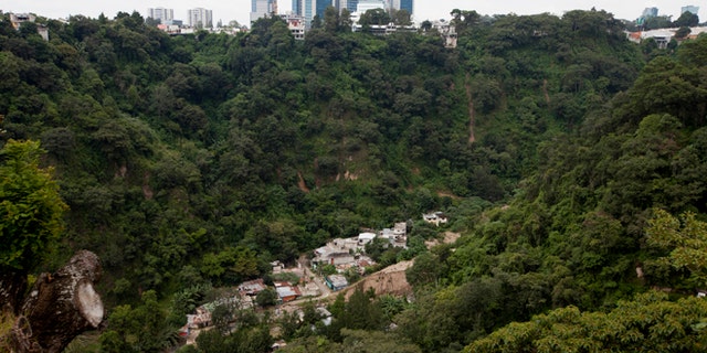This Sept. 27, 2016 photo shows the abandoned neighborhood El Cambray, bottom, seen from the the Santa Catarina Pinula cemetery where one can also see downtown Guatemala City, one year after a mudslide unleashed at least 105 million cubic feet (3 million cubic meters) of earth on the neighborhood. The official explanation is that the river that runs along the base of the hillside had been diverted into a channel that eroded the slope. (AP Photo/Moises Castillo)