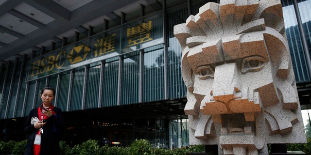 An employee of HSBC walks while checking her mobile phone in front of the HSBC building in Hong Kong Tuesday, June 9, 2015. HSBC Holdings, Britain's largest bank by market value, will cut up to 25,000 jobs around the world to reduce costs and shift its center of gravity back toward the fast-growing Asian economies where it started operations 150 years ago. Though it has not yet decided whether to move its headquarters, the bank's statement shows clearly where it thinks its commercial future lies China and the Asia-Pacific region. (AP Photo/Kin Cheung)