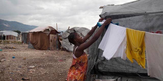 FILE - In this July 10, 2013 file photo, a woman fixes a clothes line next to her tent under cloudy skies caused by the nearby passing of Tropical Storm Chantal at the Jean-Marie Vincent camp for people displaced by the 2010 earthquake in Port-au-Prince, Haiti. A study released on Monday, April 7, 2014 finds that many of the camps are growing again, even as the overall population of quake refugees is falling. The study from the International Organization for Migration attributes the phenomenon mostly to people who have returned because they canít afford rents elsewhere. (AP Photo/Dieu Nalio Chery, File)