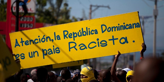 Protesters hold a banner that reads in Spanish; "Attention, the Dominican Republic is a racist country," in Port-au-Prince, Haiti, Friday, Dec. 6, 2013. Hundreds of people gathered near the Dominica Embassy decrying a recent court decision in the Dominican Republic that could strip the citizenship of generations of people of Haitian descent living in the neighboring country. (AP Photo/Dieu Nalio Chery)