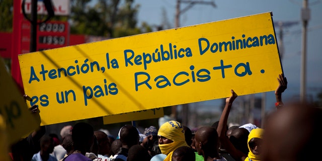 Protesters hold a banner that reads in Spanish; "Attention, the Dominican Republic is a racist country," in Port-au-Prince, Haiti, Friday, Dec. 6, 2013. Hundreds of people gathered near the Dominica Embassy decrying a recent court decision in the Dominican Republic that could strip the citizenship of generations of people of Haitian descent living in the neighboring country. (AP Photo/Dieu Nalio Chery)