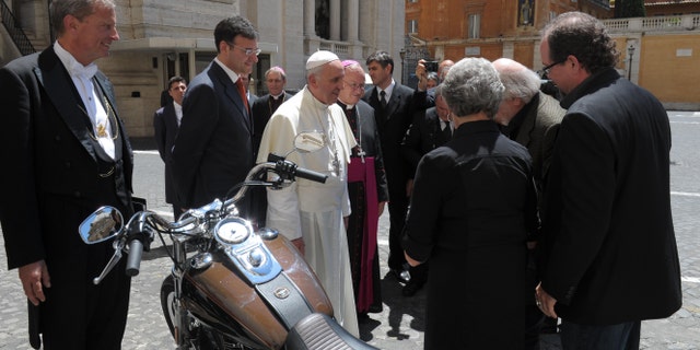 In this June 12, 2013 photo provided by the Vatican paper L'Osservatore Romano, Pope Francis stands by a Harley-Davidson he was donated, at the Vatican. A 1,585cc Harley-Davidson Dyna Super Glide, donated to Pope Francis last year and signed by him on its tank, will be sold at auction in Paris to help raise funds for a soup kitchen and hostel for the homeless in Rome. Bonhams, noting in a statement Monday Francis' "preference for modest modes of transport," says it will also be auctioning off on Feb. 6 a Harley-Davidson 110th anniversary leather motorcycle jacket, size XL, donated to and signed by Francis. The auction sales will raise money for Caritas Roma, a Catholic charity based in Rome. (AP Photo/L'Osservatore Romano)