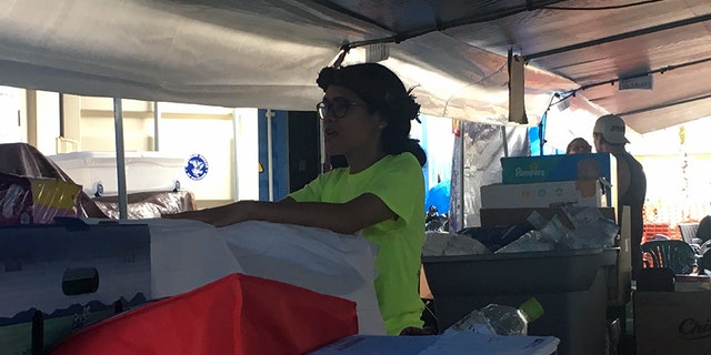Keala Martins-Keliihoomalu under a tarp tent, opening boxes of donations.