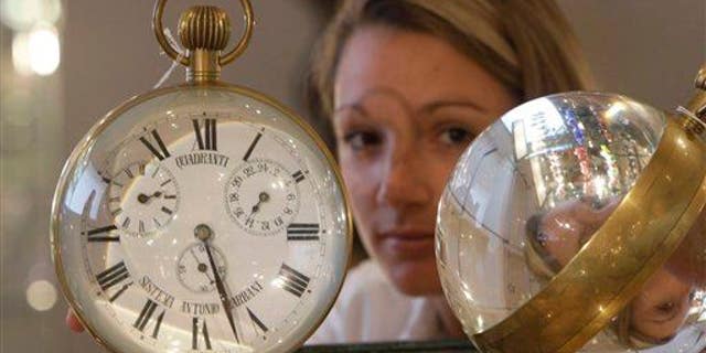 A Bonhams employee holds two Victorian glass and brass bull's-eye desktop clocks on view at Bonhams auction house in London, Monday, Sept. 28, 2009, in London.