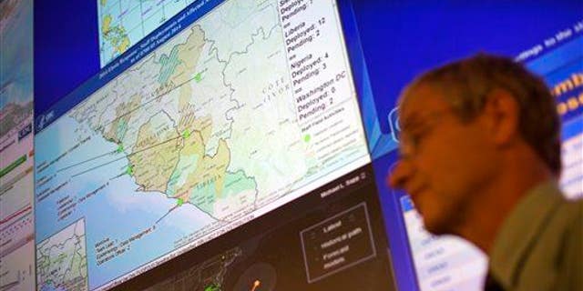 A CDC official stands under a map showing the agency's deployment of workers in West Africa at the agency's Emergency Operations Center, Tuesday, Aug. 5, 2014, in Atlanta.