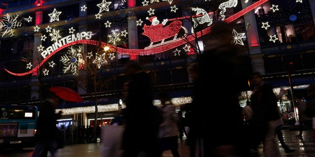 Shoppers carry bags with gifts outside a department store decorated with lights depicting Santa Claus and reindeer in Paris. Kim Komando has tips on five smartphone apps that will lead to the best deals this holiday season.
