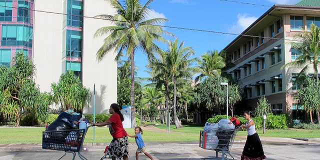 Kionina Kaneso, left, pushes carts of laundry followed by her granddaughter, Keioleen Helly, center, and daughter, Kifency Kinny, past the University of Hawaii John A. Burns School of Medicine near a tent in a homeless encampment in which they lived in Honolulu.