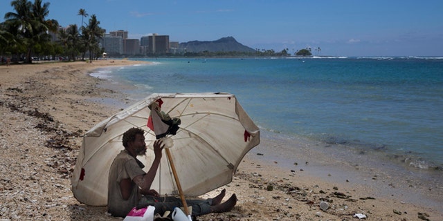 A homeless man drinks water while sitting on the beach at Ala Moana Beach Park located near Waikiki in Honolulu.