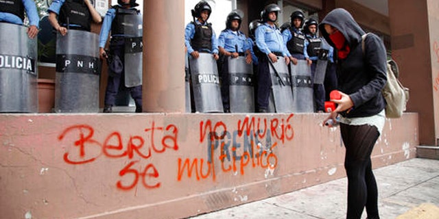 A protester writes with spray paint "Berta did not die, she multiplied" in front of riot police guarding the attorney general's office in Tegucigalpa, Honduras, Thursday, Oct. 20, 2016. Members of the Civic Council of Popular and Indigenous Organizations of Honduras (COPINH) and people belonging to the Garifuna people protested to demand justice over the March 2016 murder of Honduran indigenous leader and environmentalist Berta Caceres and to halt construction of the Agua Zarca dam, which would displace many of the indigenous Lenca people. (AP Photo/Fernando Antonio)