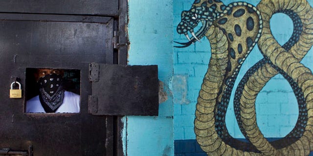 May 28, 2013: A masked member of the 18th Street gang peers from behind a window of a prison door as other gang members give a press conference inside the San Pedro Sula prison in Honduras.