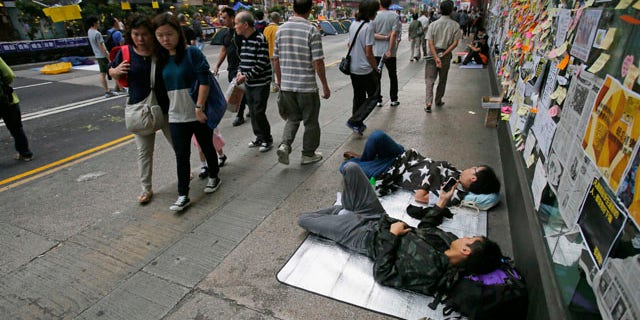 October 16, 2014: Pedestrians walk past sleeping pro-democracy students on an occupied street by the protesters in the Mong Kok district of Hong Kong. (AP Photo/Wally Santana)