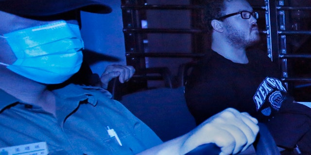 November 10, 2914: In this photo taken through tinted glass, Rurik George Caton Jutting, right, a 29-year-old British banker, is escorted by Correctional Services officers in a prison bus arriving at a court in Hong Kong. (AP Photo/Vincent Yu)