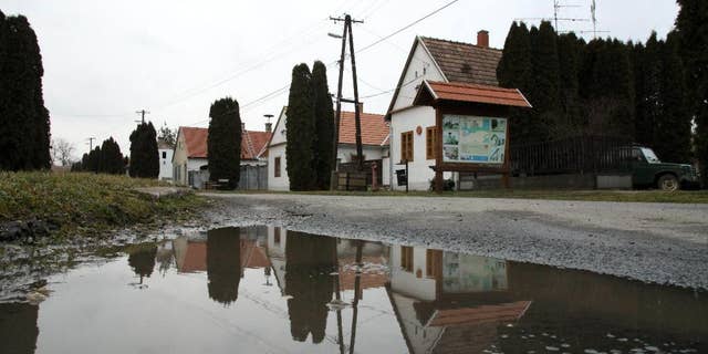 FILE - In this Wednesday, Feb. 25, 2015 file photo, houses are reflected in a puddle on the main road in the village of Megyer, Veszprem county, 190 kilometers (120 miles) southwest of Budapest, Hungary. Rooms at Hungary’s village-for-rent are going fast. Over 300 inquiries and reservations for 280 guests have been made since Mayor Kristof Pajer last week began advertising the village of Megyer, available for 210,000 forints ($760; 690 euros) a day. Pajer said Thursday, March 5, 2015, tourists are coming from as far away as Australia, South Africa, Sweden and the United States and the village “is booked solid in August and most of April and May.” (AP Photo/MTI, Lajos Nagy, File)