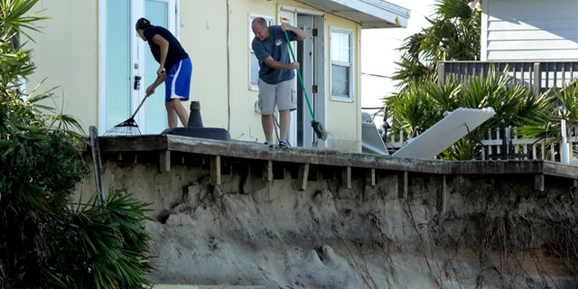 Rob Jakoby and his son Jake sweep debris off the eroded deck at his damaged beach home at Ponte Vedra Beach, Fla., Saturday, Oct. 8, 2016, after Hurricane Matthew passed through Friday. (AP Photo/Charlie Riedel)