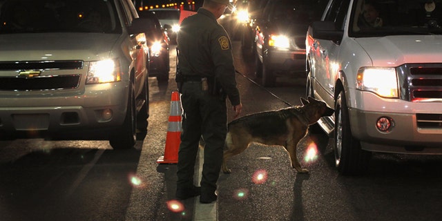NOGALES, AZ - DECEMBER 07:  A border patrol agent and Gitta, a drug-sniffing German shepherd, work a checkpoint on December 7, 2010 north of Nogales, Arizona. The checkpoint falls in the Tucson sector of the U.S.- Mexico border and is considered the most heavily trafficked by illegal immigrants and drug smugglers in the United States.  (Photo by John Moore/Getty Images)