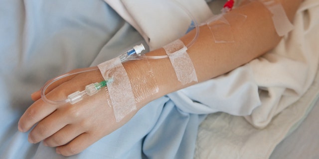 Woman in a hosptial with an IV drip in her hand and arm.