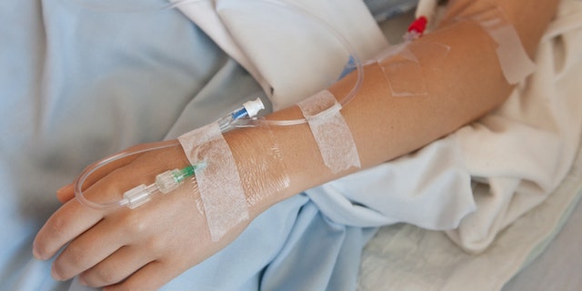 Woman in a hosptial with an IV drip in her hand and arm.