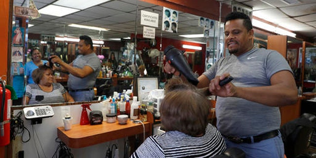 In this Wednesday, Aug. 17, 2016, photo Manolo Reyes works on a clients hair while speaking during an interview with The Associated Press in his hair salon in the Ozone Park neighborhood of the Queens borough of New York.  The shooting of an imam and his assistant near their New York mosque has unnerved Muslim residents of the Ozone Park section of Queens.   (AP Photo/Mary Altaffer)