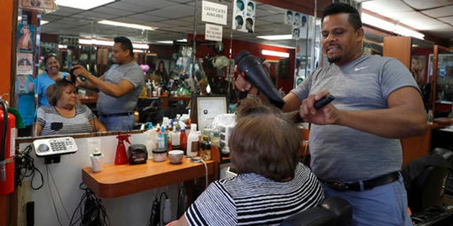 In this Wednesday, Aug. 17, 2016, photo Manolo Reyes works on a clients hair while speaking during an interview with The Associated Press in his hair salon in the Ozone Park neighborhood of the Queens borough of New York. The shooting of an imam and his assistant near their New York mosque has unnerved Muslim residents of the Ozone Park section of Queens. (AP Photo/Mary Altaffer)