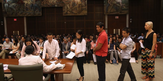 NEW YORK, NY - JUNE 21: Immigrants sign their certificates of U.S. citizenship before a naturalization ceremony on June 21, 2013 in the Brooklyn borough of New York City. Some 270 people took the oath of allegiance during a ceremony held at the Theodore Roosevelt Federal Courthouse in downtown Brooklyn. One of the busiest courthouses for naturalization ceremonies in the nation, court officials say they expect to swear in some 77,000 new American citizens in Brooklyn in 2013. In the background of the courtroom hangs a 1937 Edward Laning painting "The Role of the Immigrant in the Industrial Development of America," which was salvaged from Ellis Island. (Photo by John Moore/Getty Images)