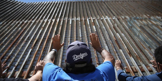 TIJUANA, MEXICO - MAY 01: Immigrant advocacy members pray at the U.S.-Mexico border fence on May 1, 2016 in Tijuana, Mexico. Mexicans on the Tijuana side can approach the border fence at any time. The U.S. Border Patrol, however, tightly controls the San Diego, CA side and allows visitors to speak to loved ones through the fence during specific weekend hours at "Friendship Park," which straddles the border. The park is the only place along the 1,954-mile border where such interactions are permitted by U.S. authorities. On only three occassions have U.S. officials allowed a gate to be opened at the park for pre-screened separated family members to embrace. (Photo by John Moore/Getty Images)