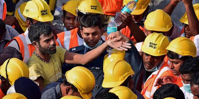 In this Tuesday, July 1, 2014 photograph, India’s National Disaster Response Force personnel stand around a man, left, they rescued from beneath the debris of a building that collapsed Saturday on the outskirts of Chennai, India. Rescuers pulled seven more survivors from under the concrete ruins of a collapsed 11-story building on Tuesday, three days after it toppled and killed dozens of people in southern India, officials said. (AP Photo)