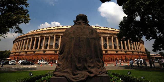 A statue of Mahatma Gandhi overlooks the Indian Parliament house on the opening day of its monsoon session, in New Delhi, India, Tuesday, July 21, 2015. (AP Photo/ Manish Swarup)