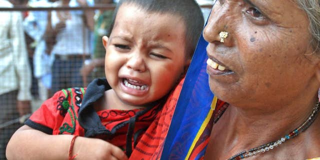 A woman holds a crying child as relatives of victims gather at the spot of a stampede at the Kamta Nath Hindu temple in Chitrakoot, India, Monday, Aug. 25, 2014. A pre-dawn stampede killed 10 people Monday as tens of thousands of Hindus were worshipping in an annual procession marking the holy day of Somvati Amavasya. (AP Photo/Amar Deep)