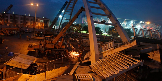 September 21: Indian workers remove debris from a collapsed bridge near an illuminated Jawaharlal Nehru stadium in New Delhi, India.  A footbridge under construction near the Commonwealth Games main stadium collapsed on Tuesday, injuring people, police said. The games are scheduled to be held from Oct. 3-14. (AP)