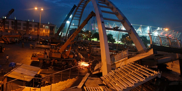 September 21: Indian workers remove debris from a collapsed bridge near an illuminated Jawaharlal Nehru stadium in New Delhi, India. A footbridge under construction near the Commonwealth Games main stadium collapsed on Tuesday, injuring people, police said. The games are scheduled to be held from Oct. 3-14. (AP)