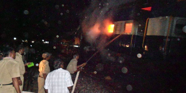 May 22, 2012: Firefighters and policemen try to douse flames on a train after an accident at a station near Penukonda.
