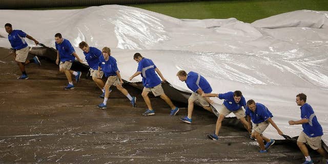 Members of the grounds crew  pull the tarp on the field during a rain delay in the 10th inning of a baseball game between the Kansas City Royals and the Cleveland Indians Sunday, Aug. 31, 2014, in Kansas City, Mo. (AP Photo/Charlie Riedel)